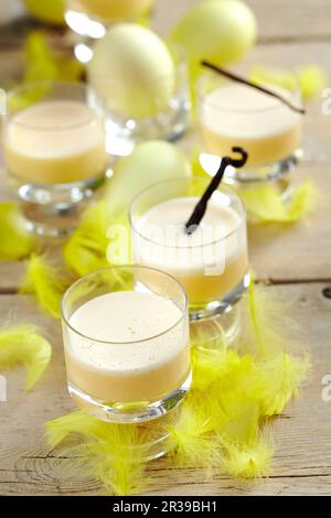 Osterbrille mit Vanille-Eierpunsch, dekoriert mit gelben Federn und Ostereiern Stockfoto