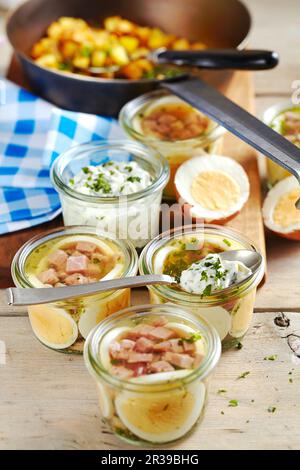 Schinken mit gekochten Eiern in Steingläsern, mit Remulade und gebratenen Kartoffeln Stockfoto