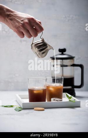 Eine Frau gießt Mandelmilch in eiskalten Kaffee Stockfoto