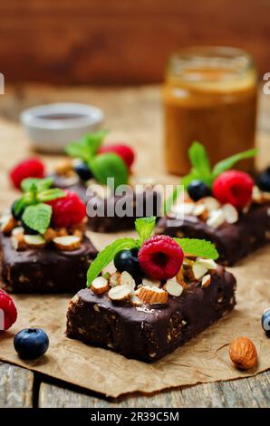 Rohe vegane Schokolade ohne Backen, Datteln und Mandelbrownies mit Schokoladenzuckercreme und Beeren Stockfoto