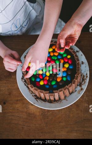 Kinderhände dekorieren einen Kuchen mit bunten Süßigkeiten Stockfoto