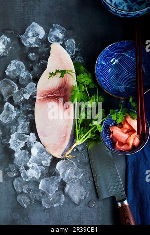 Schwertfischsteak auf Eis neben Koriander, einem Messer und einer orientalischen Schüssel Stockfoto