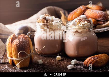 Heiße Schokolade mit Schlagsahne und Marshmallows serviert mit Madeleines Stockfoto