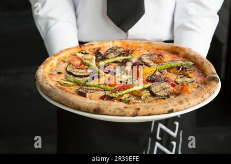 Kellner in Uniform mit Gemüsepizza Stockfoto