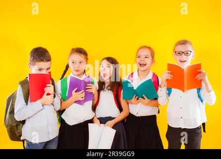 Fröhliche lächelnde kleine Studenten halten Farbbücher isoliert auf gelbem Hintergrund. Zurück zur Schule. Stockfoto