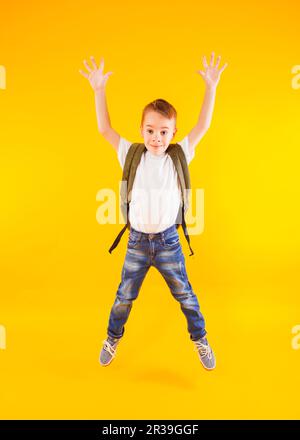 Glückliches Kind springt mit Rucksack über gelben Hintergrund zurück zur Schule Stockfoto