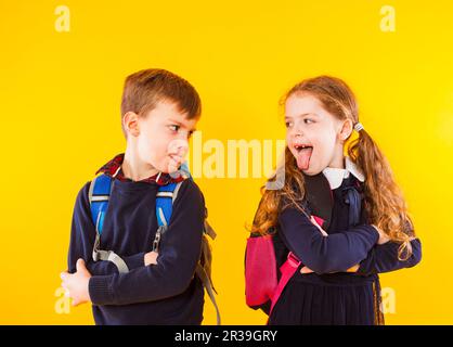 Lustige Kinder in Schuluniform haben Spaß zusammen. Kinder zeigen sich gegenseitig Zunge Stockfoto