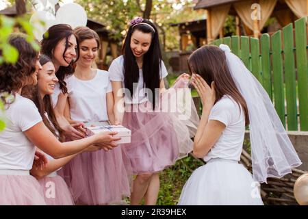 Glückliche Freundinnen, die der Braut auf der Hühnerparty ein Geschenk machen Stockfoto