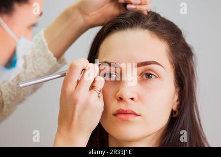 Master Makeup korrigiert Augenbrauen in einem Schönheitssalon und verleiht ihm Form Stockfoto