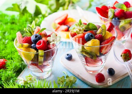 Gesundes frisches Obst und Beerensalat mit Erdbeeren, Himbeeren, Kiwi, Ananas, Blaubeeren und Wassermelone auf einem Tisch im Freien Stockfoto