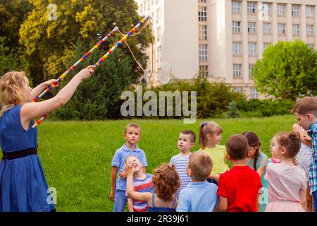 Junge Frau unterhält Kinder mit Seifenblasen Stockfoto