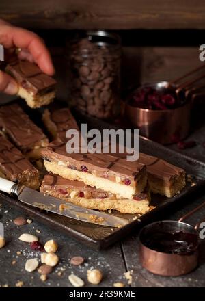 Person, die Ein Stück Karamell-Shortbread mit getrockneten Früchten und Nüssen nimmt Stockfoto