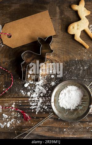 Weihnachtlicher Baby-Hirsch-Keks mit Keksschneider und Puderzucker im Sieb und Geschenkanhänger Stockfoto