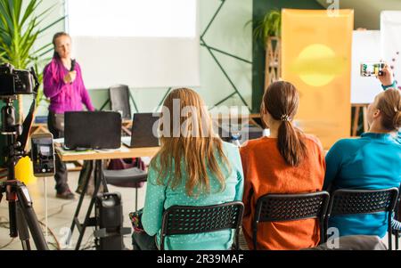 Weibliche Referentin, die bei einem Workshop vorspricht. Aufzeichnen eines Vortrags auf einem Mobiltelefon und einer Kamera. Stockfoto