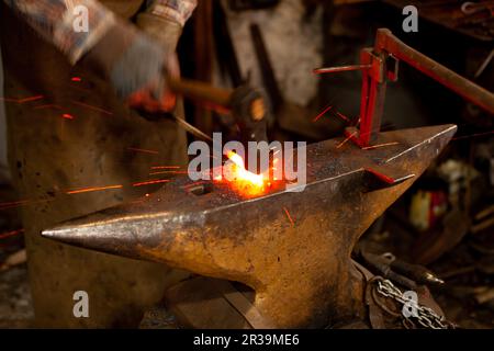 Der Schmied schmiedete das geschmolzene Metall auf dem Amboss manuell in Schmiede. Stockfoto