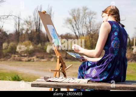 Junge Frau kreativer Maler zeichnet im Freien Pinsel-Aquarelle auf Leinwand. Inspiration für den Frühling. Stockfoto