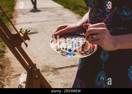 Künstler mischen Acrylpanits auf Palette. Mädchen malt ein Bild im Freien. Stockfoto