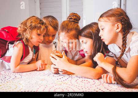 Eine Gruppe von Schulkindern mit Smartphone, die Spaß am Pausenbetrieb im Klassenzimmer haben Stockfoto