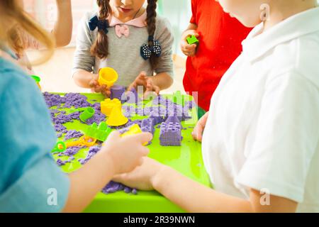 Kinder, die Plastikformen zum Spielen mit kinetischem Sand verwenden Stockfoto