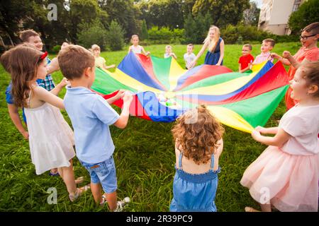 Glückliche Kinder, die während des lustigen Spiels einen Fallschirm halten Stockfoto