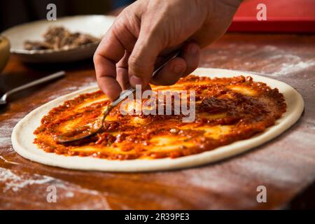 Tomatensoße zur Pizza hinzufügen Stockfoto
