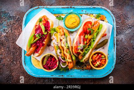 Verschiedene köstliche Hot Dogs mit Gemüse und Saucen auf einem klassischen Serviertablett. Blick von oben. Stockfoto