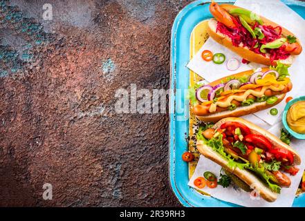 Verschiedene köstliche Hot Dogs mit Gemüse und Saucen auf einem klassischen Serviertablett. Blick von oben. Stockfoto