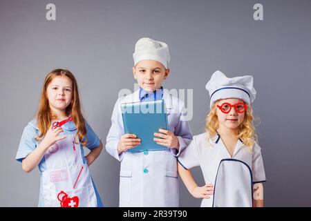 Kinder stellen sich einen zukünftigen Beruf vor. Niedliche kleine Ärzte auf grauem Hintergrund. Stockfoto