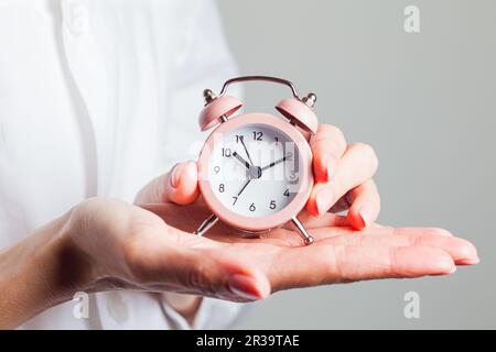 Frau in weißem Hemd hält Wecker Stockfoto
