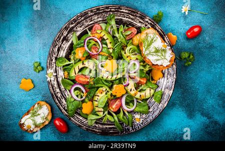 Für gesunde Ernährung: Salat mit gegrillter Avocado, frisches Gemüse, Toast mit Weichkäse und Senfdressing. Draufsicht Stockfoto