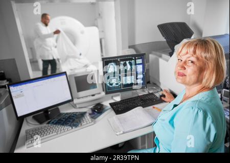 Medizinische Computertomographie oder MRT-Scanner. Porträt einer Krankenschwester, die am Computer arbeitet und ein MRT macht. Eine Frau in blauer Uniform. Konzept von Medizin und Krankenhaus. Stockfoto