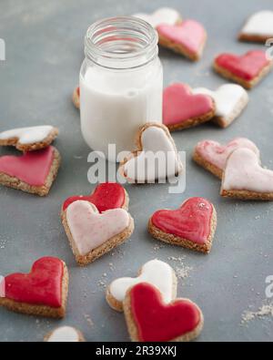 Rosafarbene, rote und weiße herzförmige Kekse mit einem Glas Milch Stockfoto