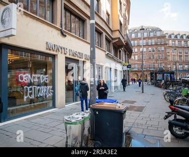 Straßburg, Frankreich - 20. März 2023: Beschädigte Fassade der Monte Paschi Banque nach einem Protest gegen die staatliche Rentenreform in Frankreich auf einer Straße in der Stadt, mit Schildern und Aufklebern an den Fassaden der Geschäfte in der Innenstadt und den Abfalleimern. Stockfoto