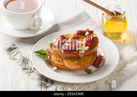 Süßer und köstlicher französischer Toast mit Rhabarber, Pistazien und Honig aus nächster Nähe auf einem Teller auf einem Holztisch. Horizontal Stockfoto