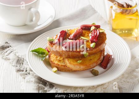 Getoasteter, heißer französischer Toast mit gebackenem Rhabarber, Pistazien und Honig aus nächster Nähe auf einem Holztisch. Horizontal Stockfoto