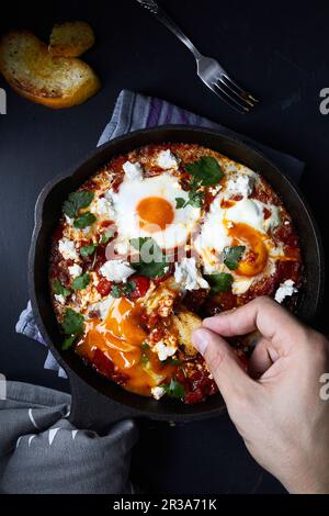 Shakshuka mit Tomaten, Paprika, Zwiebeln und Eiern, zubereitet in gusseiserner Pfanne Stockfoto