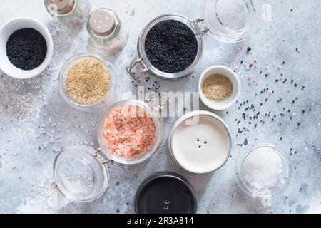 Mischung verschiedener Salztypen auf grauem Betonhintergrund. Meersalze, schwarzes und rosafarbenes Salz des Himalaya cr Stockfoto