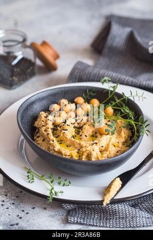 Kichererbsen Hummus in der schwarzen Schüssel, dekoriert mit Sesamsamen und Kichererbsen-Grüns. Vegane Rezepte, Stockfoto