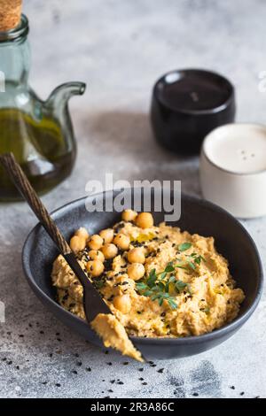 Kichererbsen Hummus in der schwarzen Schüssel, dekoriert mit Sesamsamen und Kichererbsen-Grüns. Vegane Rezepte, Stockfoto