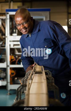 Schwarzer afrikanischer Vorgesetzter, der eine Maschine an einer Montagelinie einer Verpackungsfabrik überprüft Stockfoto