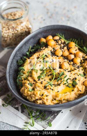 Kichererbsen Hummus in der schwarzen Schüssel, dekoriert mit Sesamsamen und Kichererbsen-Grüns. Vegane Rezepte, Stockfoto