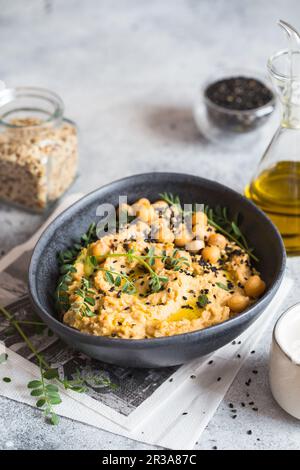 Kichererbsen Hummus in der schwarzen Schüssel, dekoriert mit Sesamsamen und Kichererbsen-Grüns. Vegane Rezepte, Stockfoto