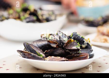 Gedünstete Muscheln in Käsesauce. Muscheln in Schalen in der Schüssel mit Weißwein auf dem Tisch. Stockfoto