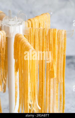 Hausgemachte Pasta Linguine, die zum Trocknen auf dem Regal hängt. Hausgemachte italienische Tagliatelle, die an einer Pasta dryi hängt Stockfoto