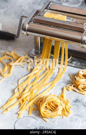 Nudelautomat aus Metall mit Teig. Fettuccine kommt aus einer manuellen Nudelmaschine. Nudeln mit p machen Stockfoto