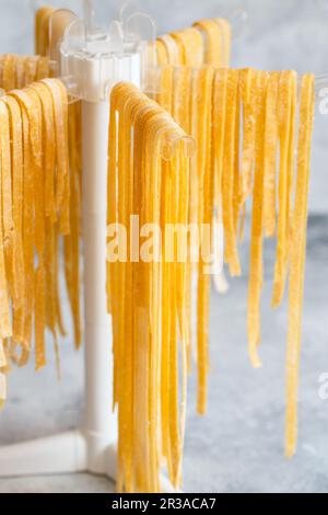 Hausgemachte Pasta Linguine, die zum Trocknen auf dem Regal hängt. Hausgemachte italienische Tagliatelle, die an einer Pasta dryi hängt Stockfoto