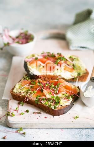 Toast mit Avocado-Creme und geräuchertem Lachs auf dem weißen Holzbrett. Geräucherter Lachs, Frischkäse und Stockfoto