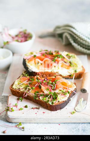 Konzept der gesunden Ernährung. Toast mit Avocado-Creme und geräuchertem Lachs auf dem weißen Holzbrett. Geraucht Stockfoto