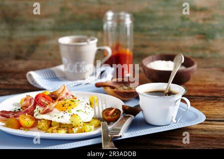 Bratkartoffeln, Speck, Spiegelei und Tomaten und Frühstück mit Kaffee Stockfoto