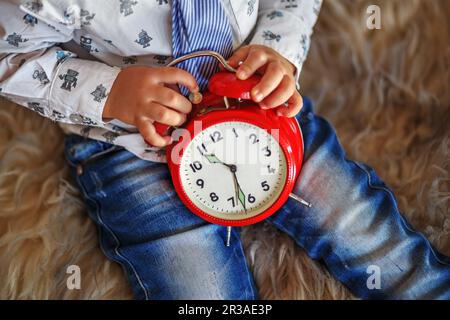 Ein kleiner Junge mit einer großen roten Uhr wartet auf Wunder. Zeitkonzept Stockfoto